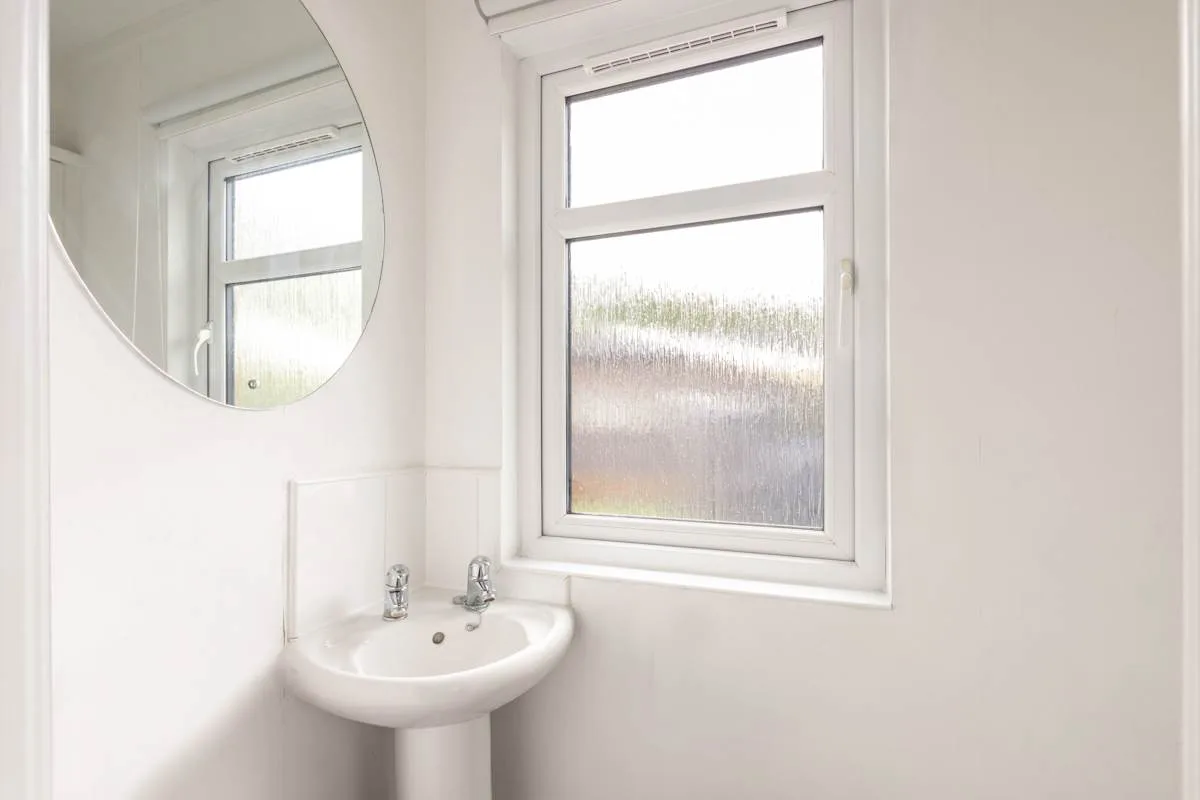 Un baño luminoso con lavabo de pedestal, espejo redondo y ventana.