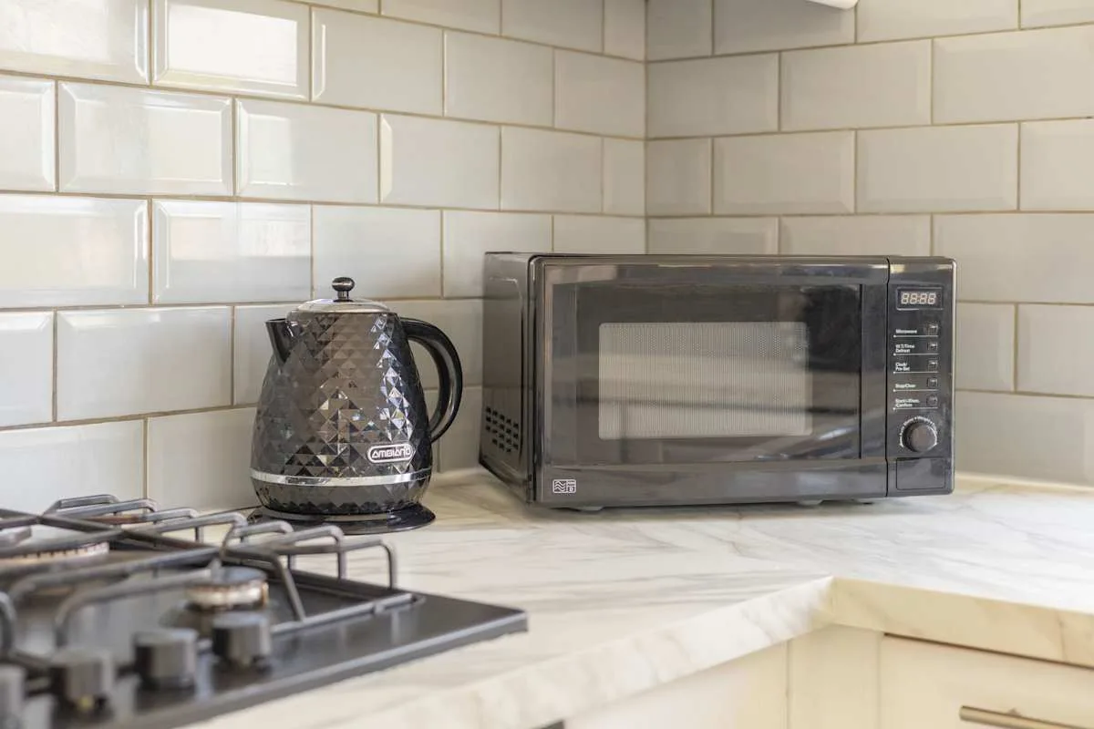 Una encimera de cocina con un microondas y un hervidor junto a la estufa.