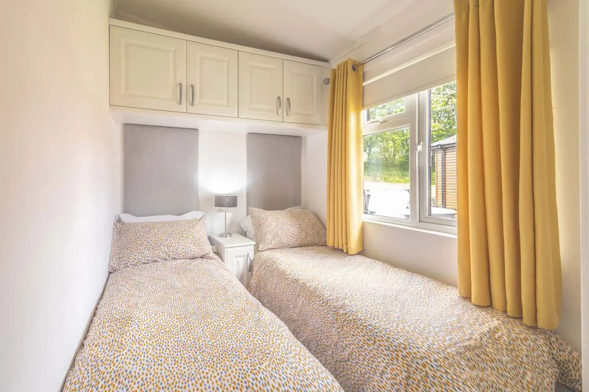 Un dormitorio luminoso con dos camas, armarios superiores y una ventana grande.