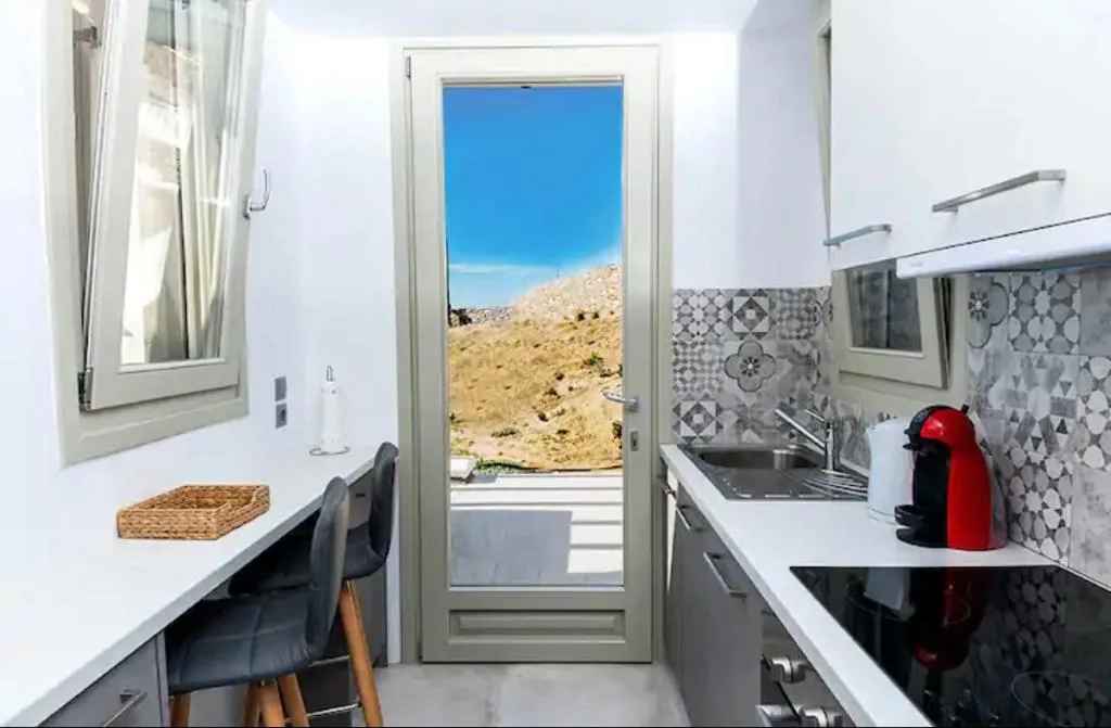 Una cocina compacta con encimera, fregadero y vistas a las colinas desde la puerta.