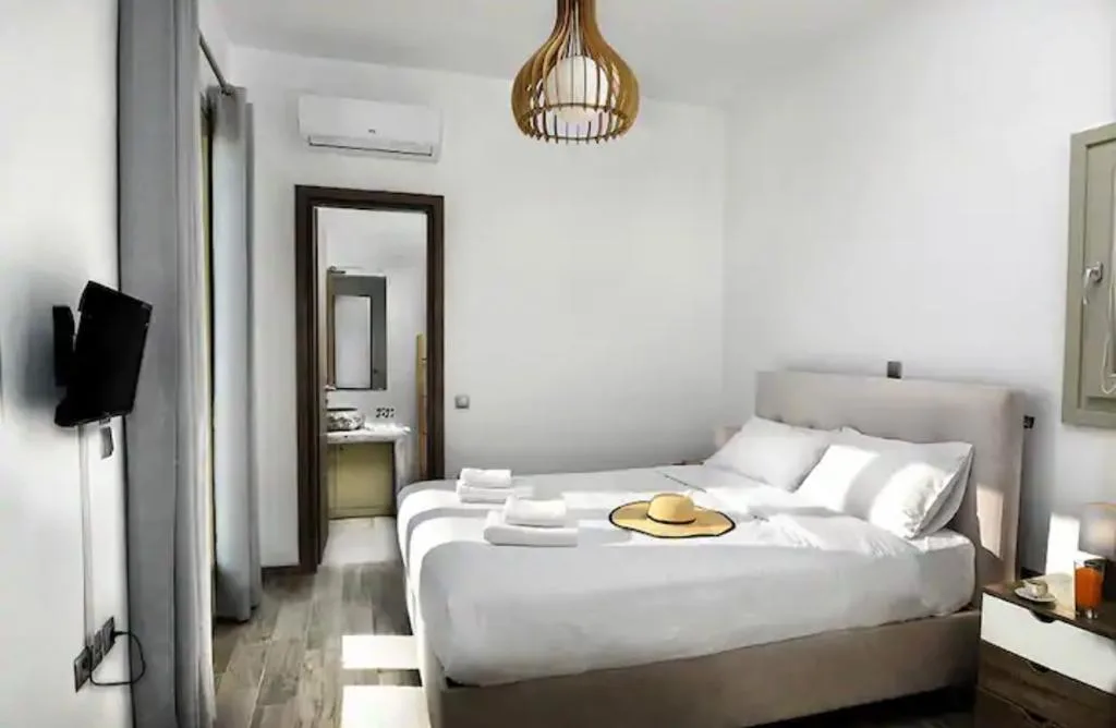 Un dormitorio luminoso con una cama bien tendida y un televisor montado en la pared.