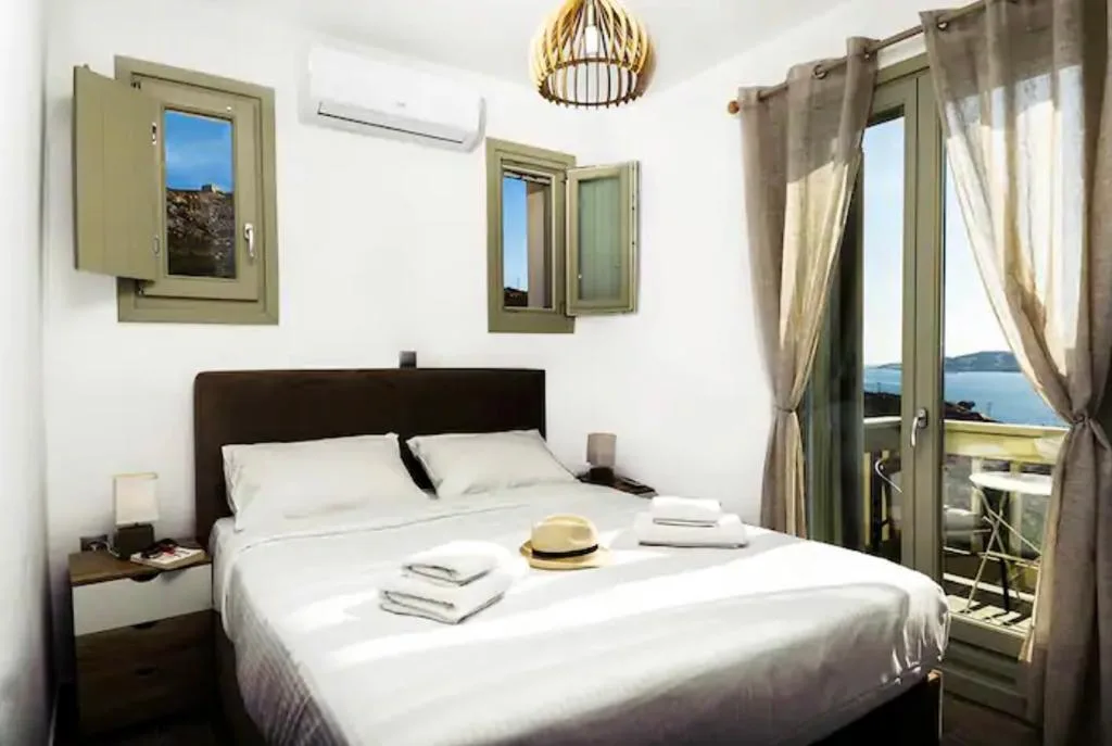 Un dormitorio luminoso con una cama bien arreglada y puertas de vidrio que dan a un balcón.