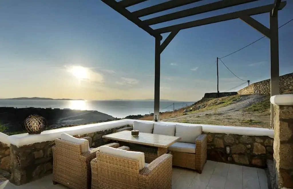 Una terraza al aire libre con asientos de mimbre mira al mar al atardecer.