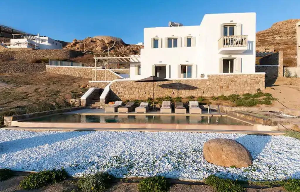 Una villa blanca se alza detrás de una piscina en un paisaje rocoso.