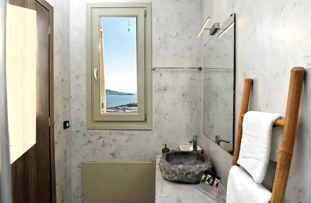 Un baño con un lavabo de piedra y una ventana con vistas al agua.