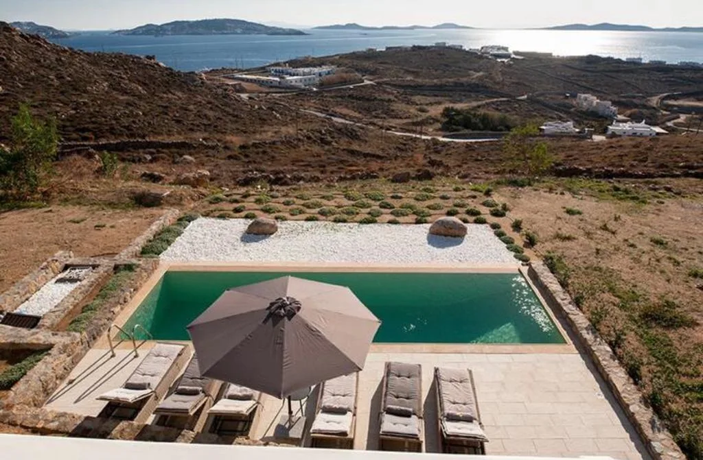 Una piscina exterior y una zona de descanso dan a un paisaje costero seco y al mar.