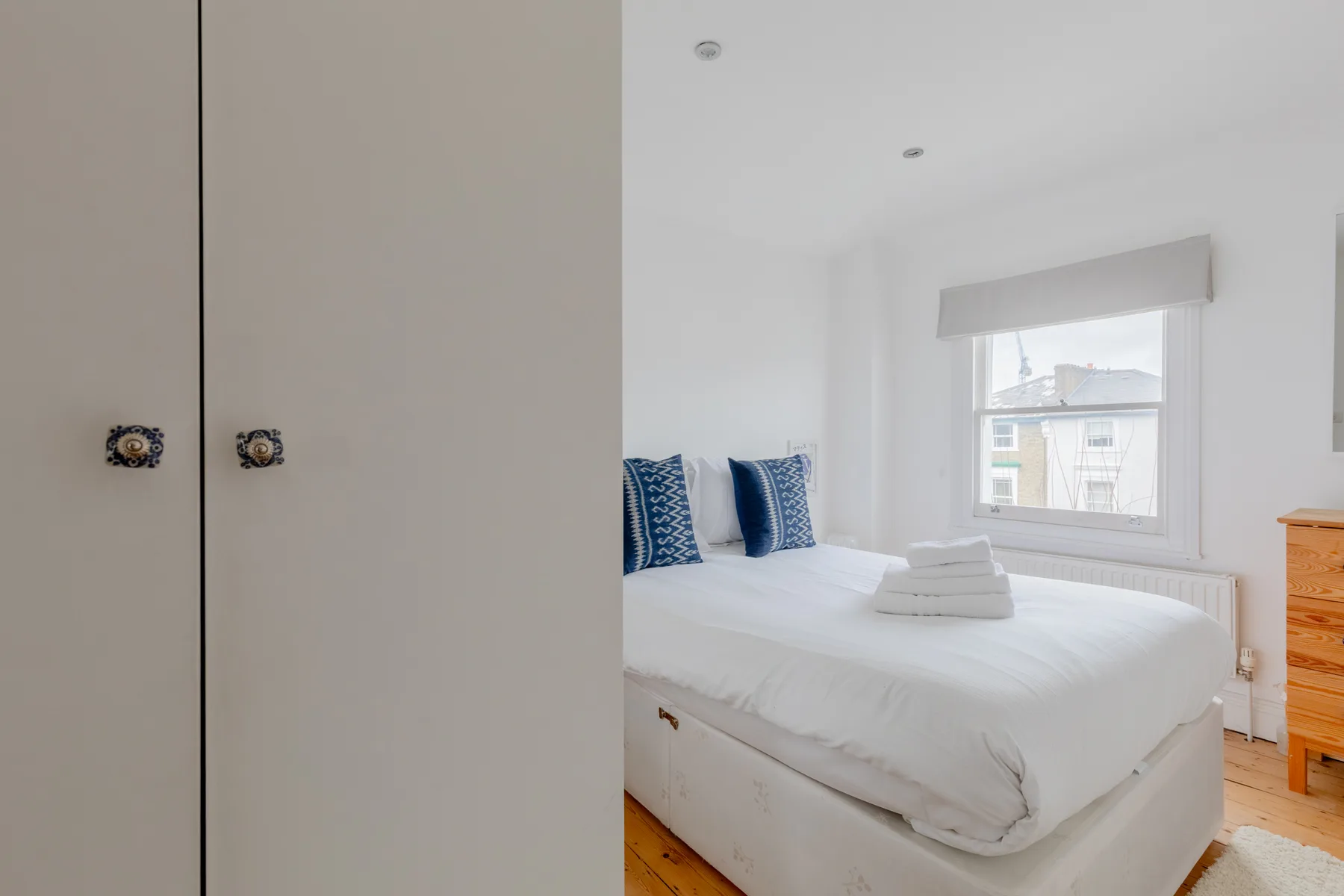 A bright bedroom with a white bed and blue pillows beside a window.