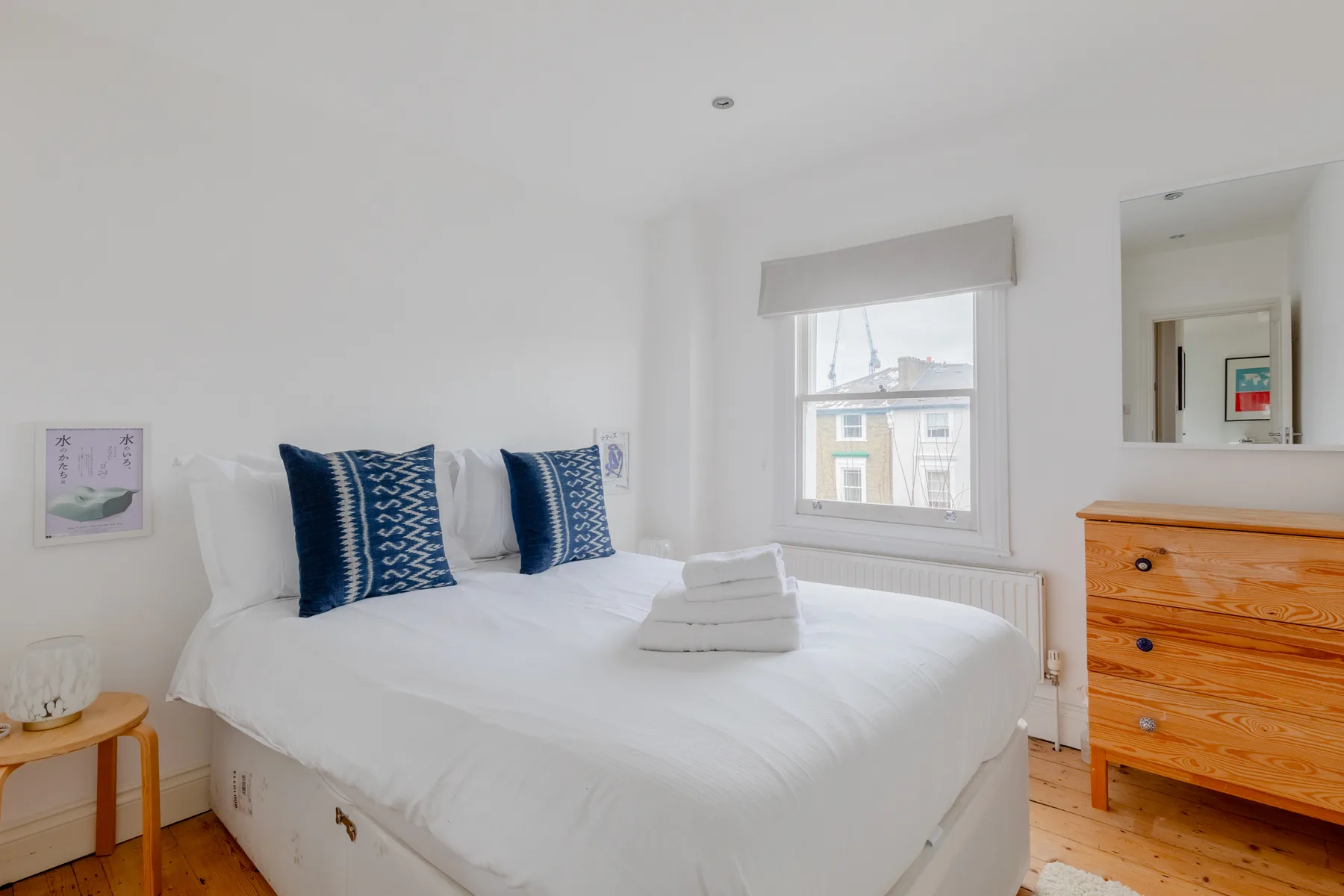 A bright bedroom with a neatly made bed and a wooden dresser.