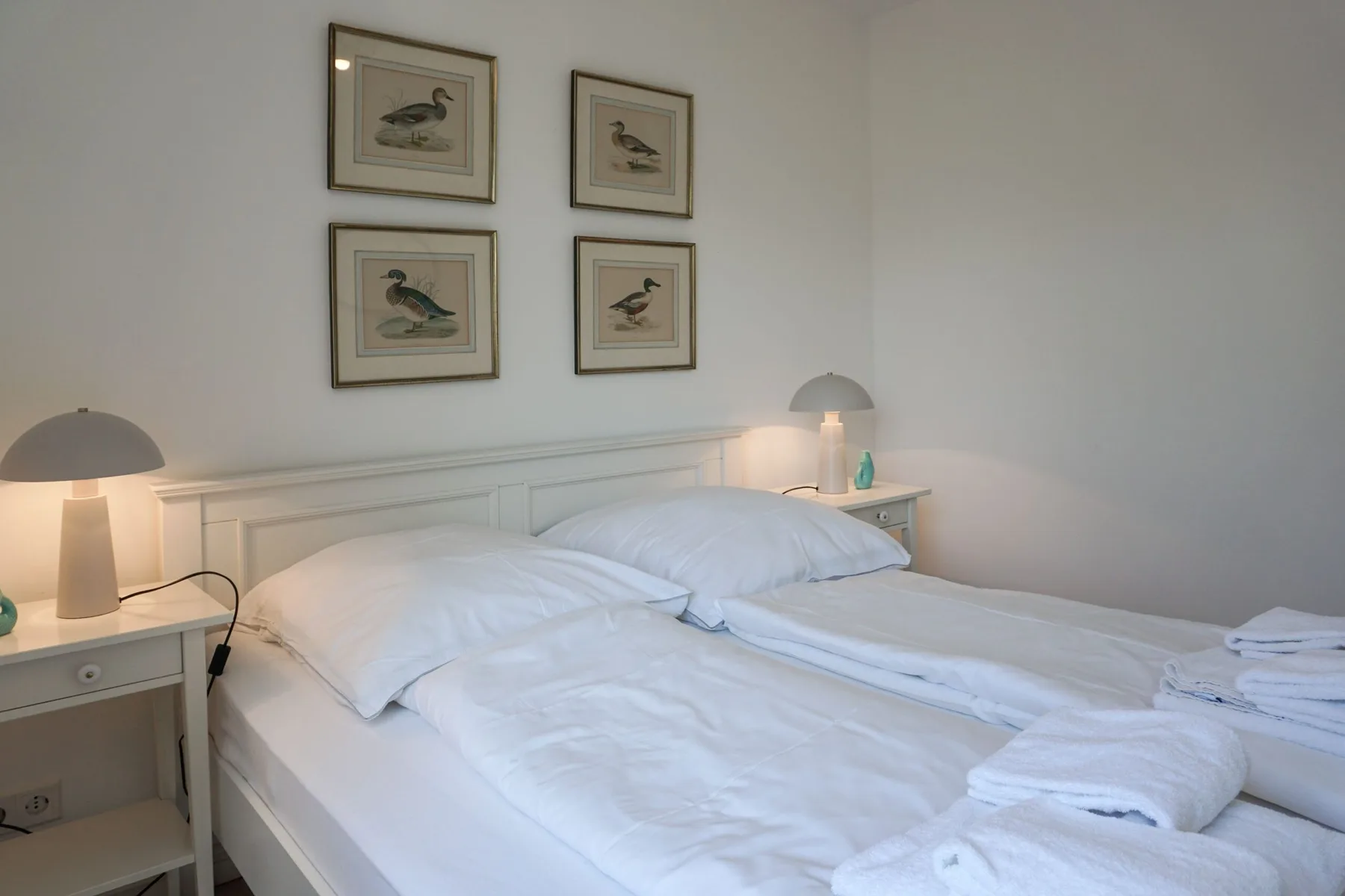 Un dormitorio con dos camas, láminas de aves enmarcadas y lámparas de mesilla.