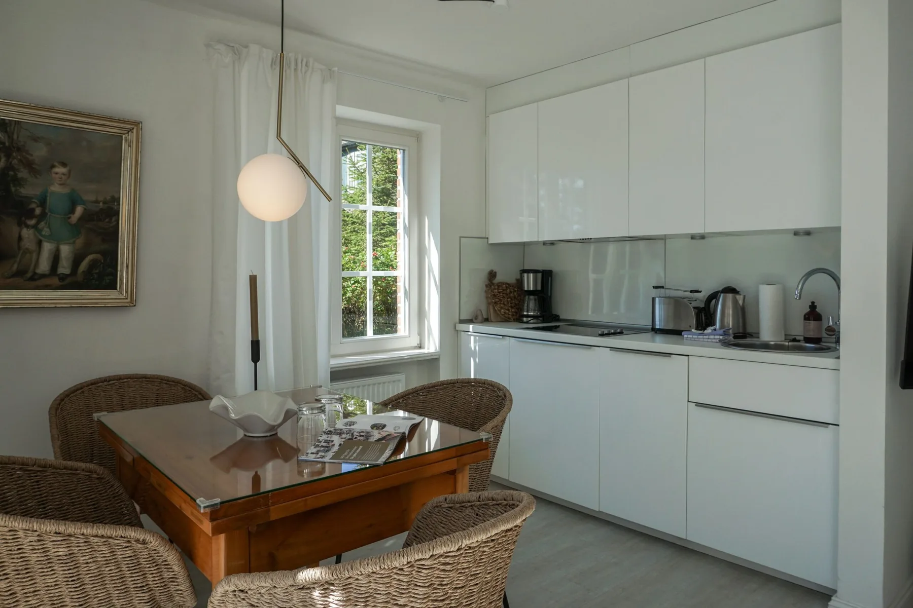 Comedor junto a una cocina compacta, con una mesa de madera y asientos de mimbre.