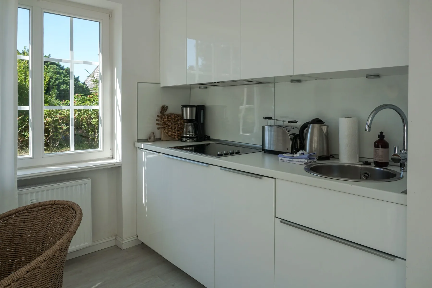 Una cocina blanca y luminosa con una ventana que da a la vegetación.