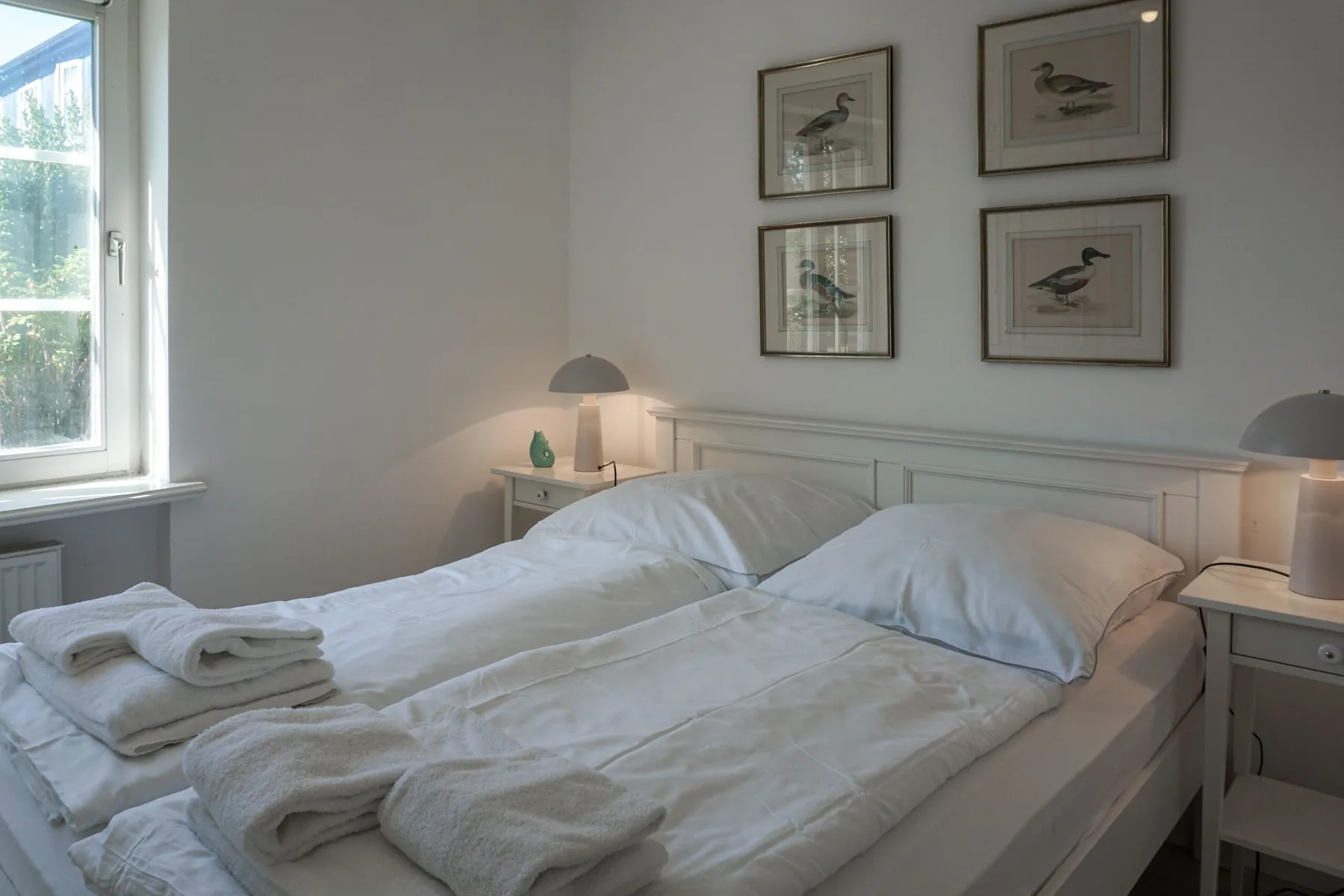Un dormitorio luminoso con cama doble, mesitas de noche y láminas de aves enmarcadas.