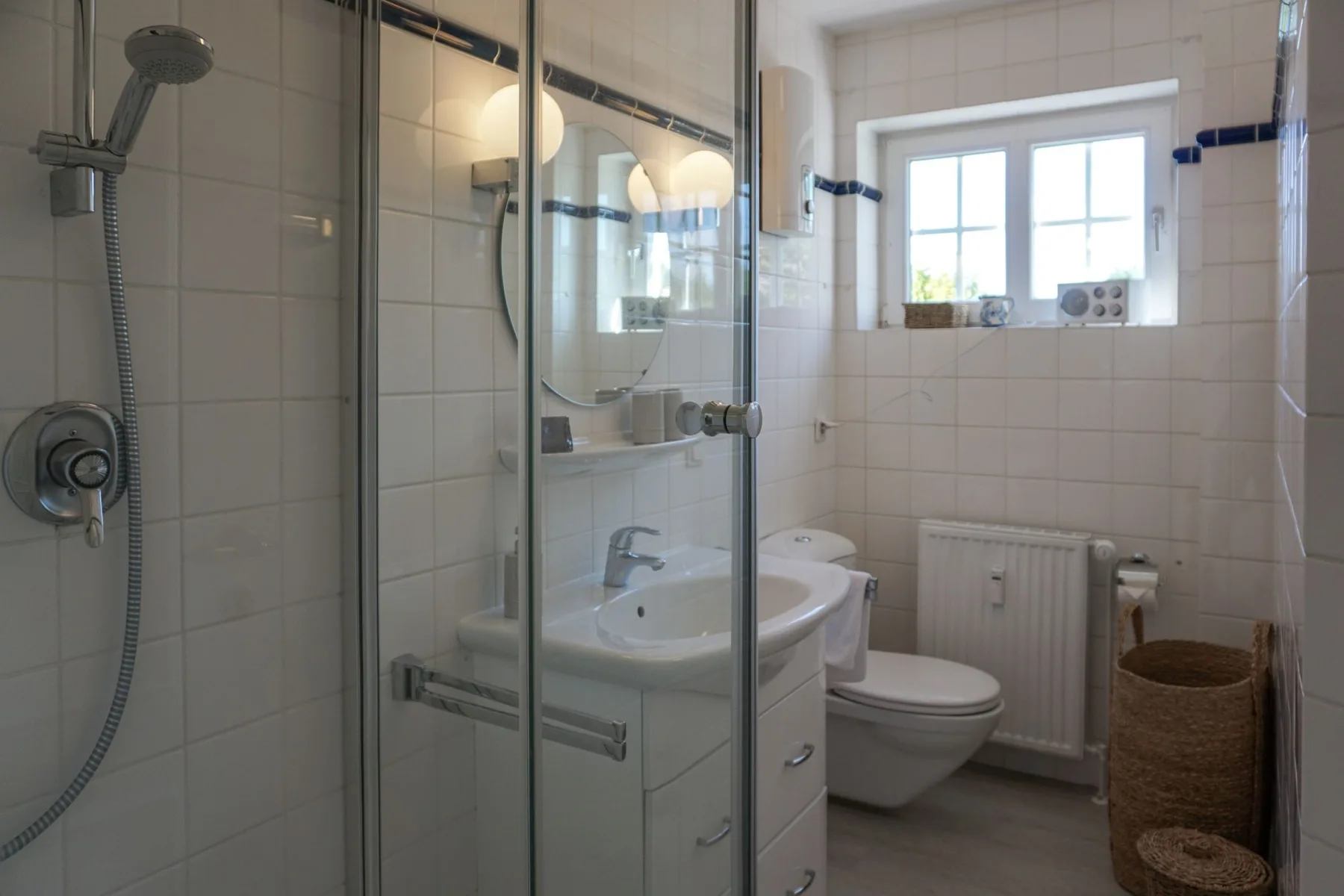 Un baño alicatado con ducha de vidrio, lavabo y ventana.