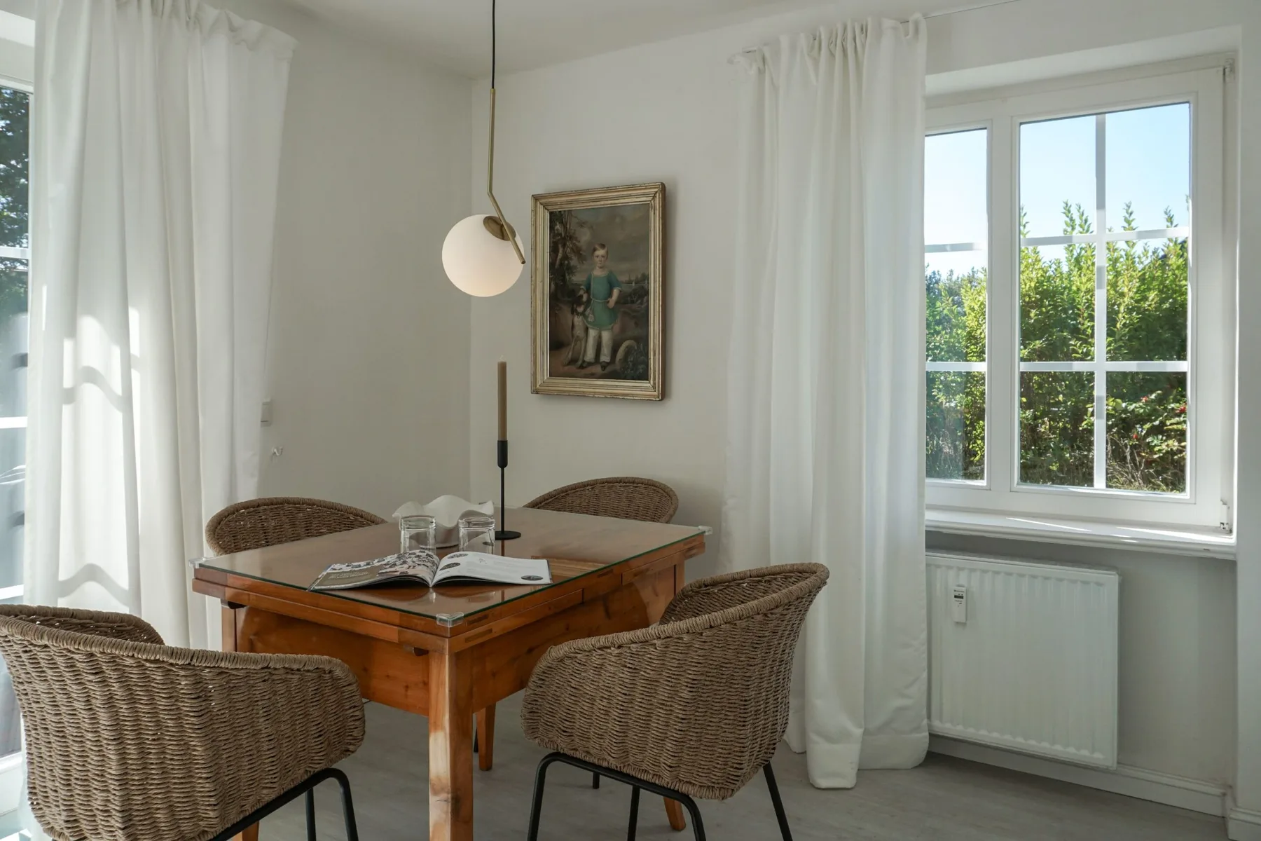 Un comedor luminoso con una mesa de madera, asientos tejidos y cortinas blancas.