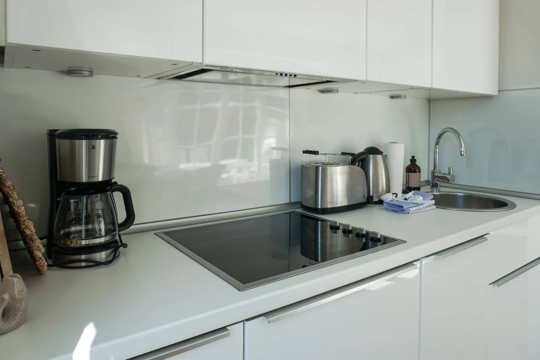 Una encimera de cocina moderna con placa de cocción, cafetera, hervidor y fregadero.