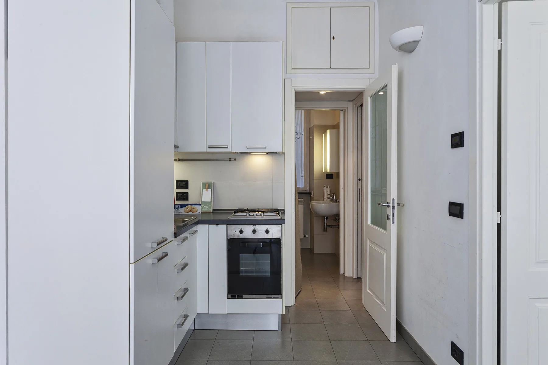 A narrow kitchen with white cabinetry, a cooktop, and an oven.