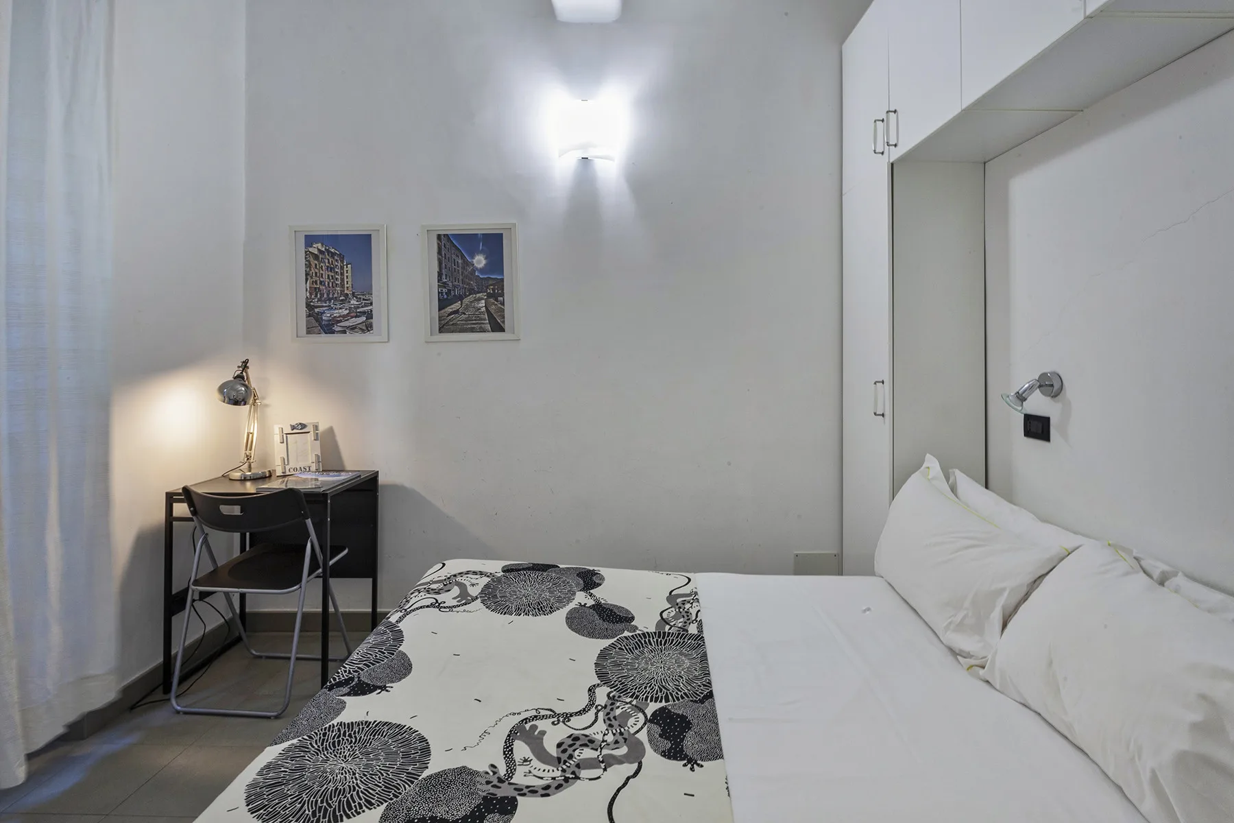 Un dormitorio con una cama, una colcha estampada y un escritorio bajo dos cuadros.