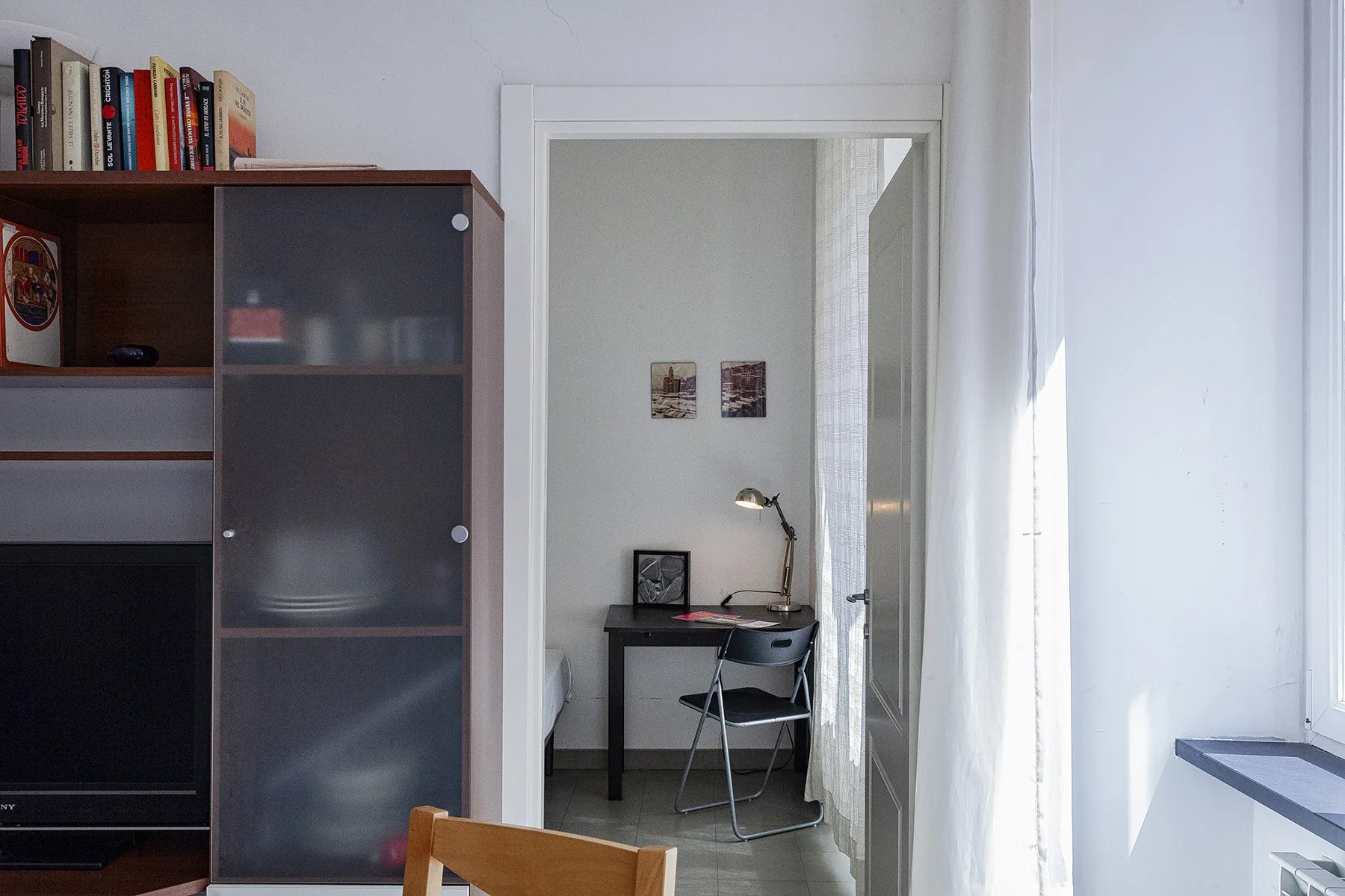 Una habitación luminosa con un escritorio y una silla junto a un armario alto.