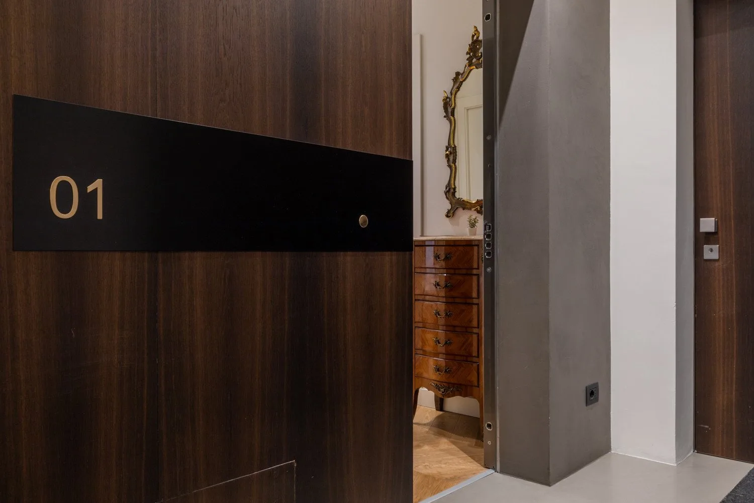 Una puerta con paneles de madera se abre a un pasillo con una cómoda y un espejo.