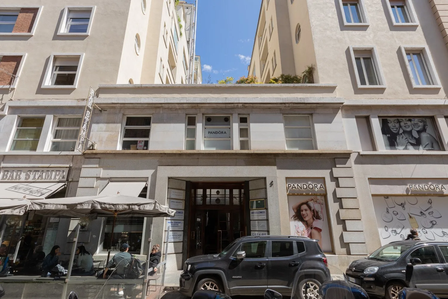 Fachada de un edificio a nivel de calle, con escaparates, una entrada y coches aparcados.