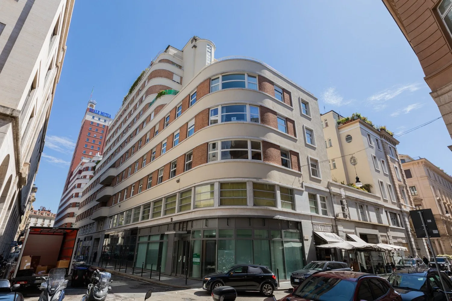 Un edificio redondeado de varios pisos se alza en una calle urbana bajo un cielo despejado.