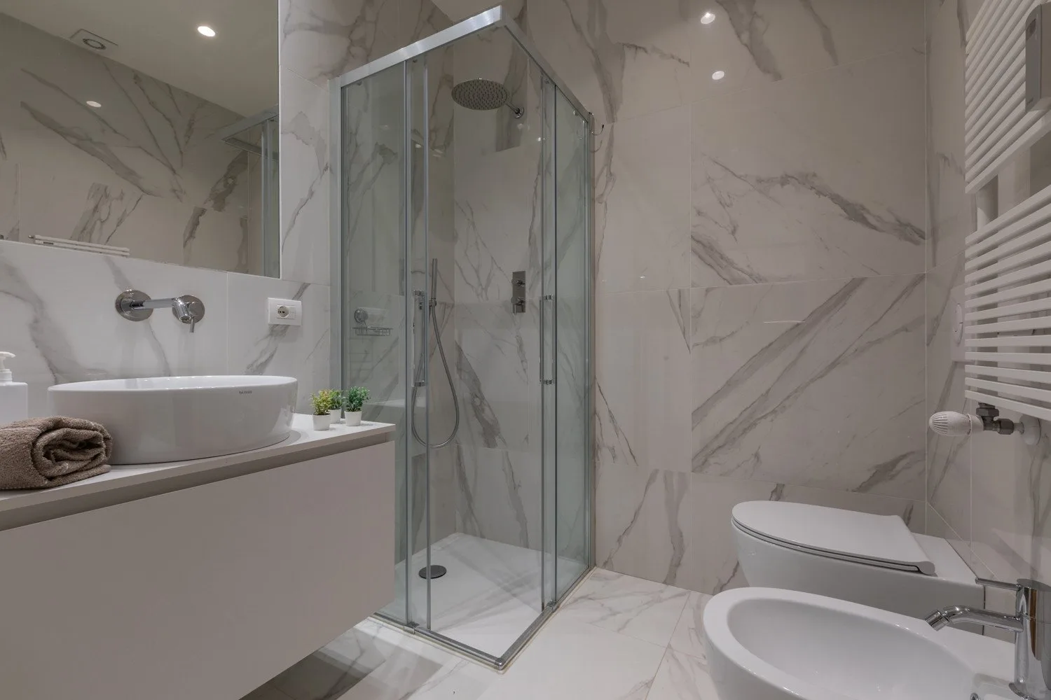 Baño revestido de mármol con ducha de vidrio, lavabo e inodoro.