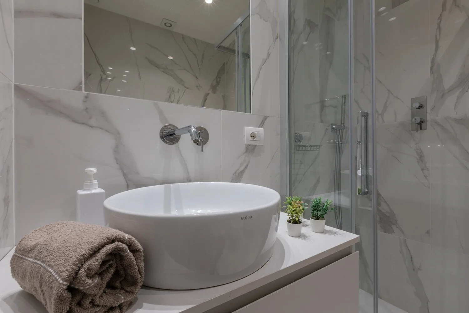 Un tocador de baño moderno con lavabo sobre encimera y ducha de vidrio.