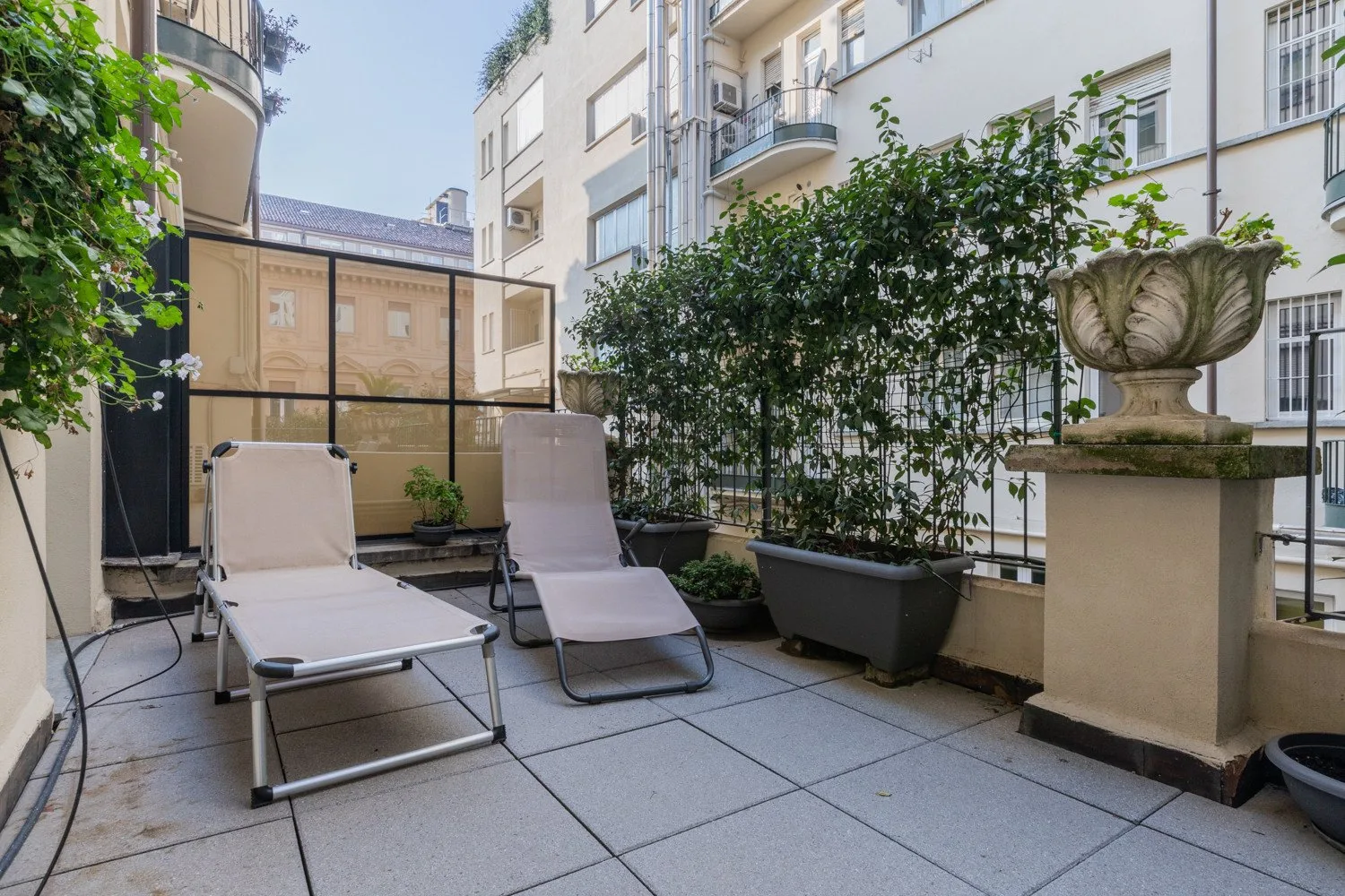 Una terraza pavimentada al aire libre con asientos reclinables y plantas en macetas.