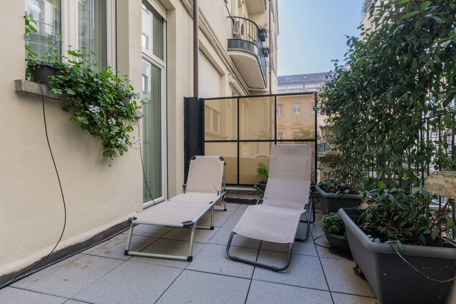 Una terraza pavimentada con asientos reclinables y plantas en macetas.