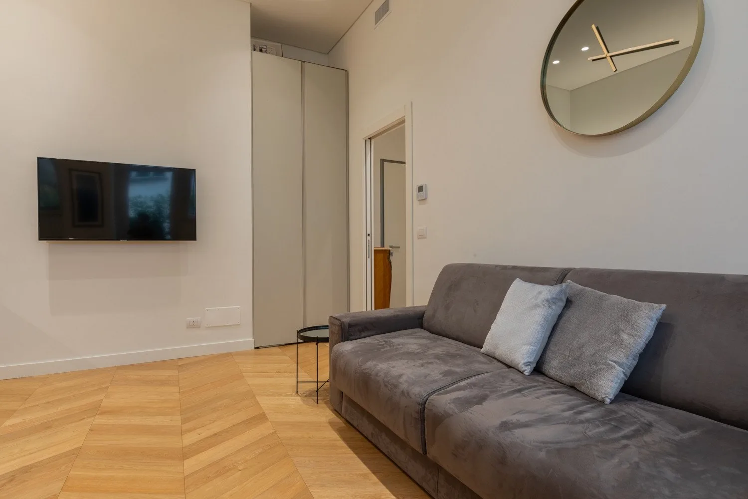 Una sala de estar con asientos grises y un televisor montado en la pared.