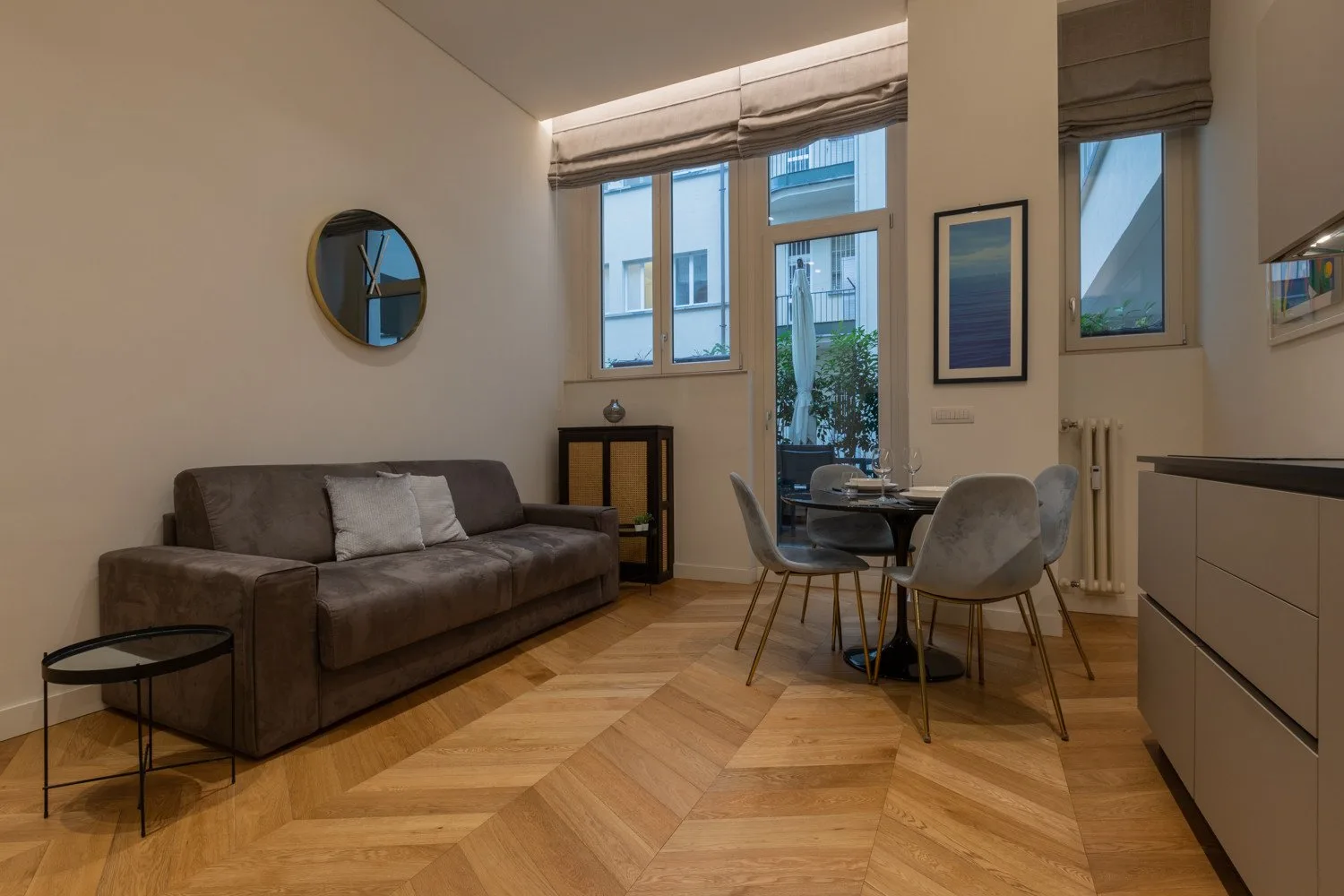 Una sala de estar con asientos y una mesa de comedor junto a ventanas altas.