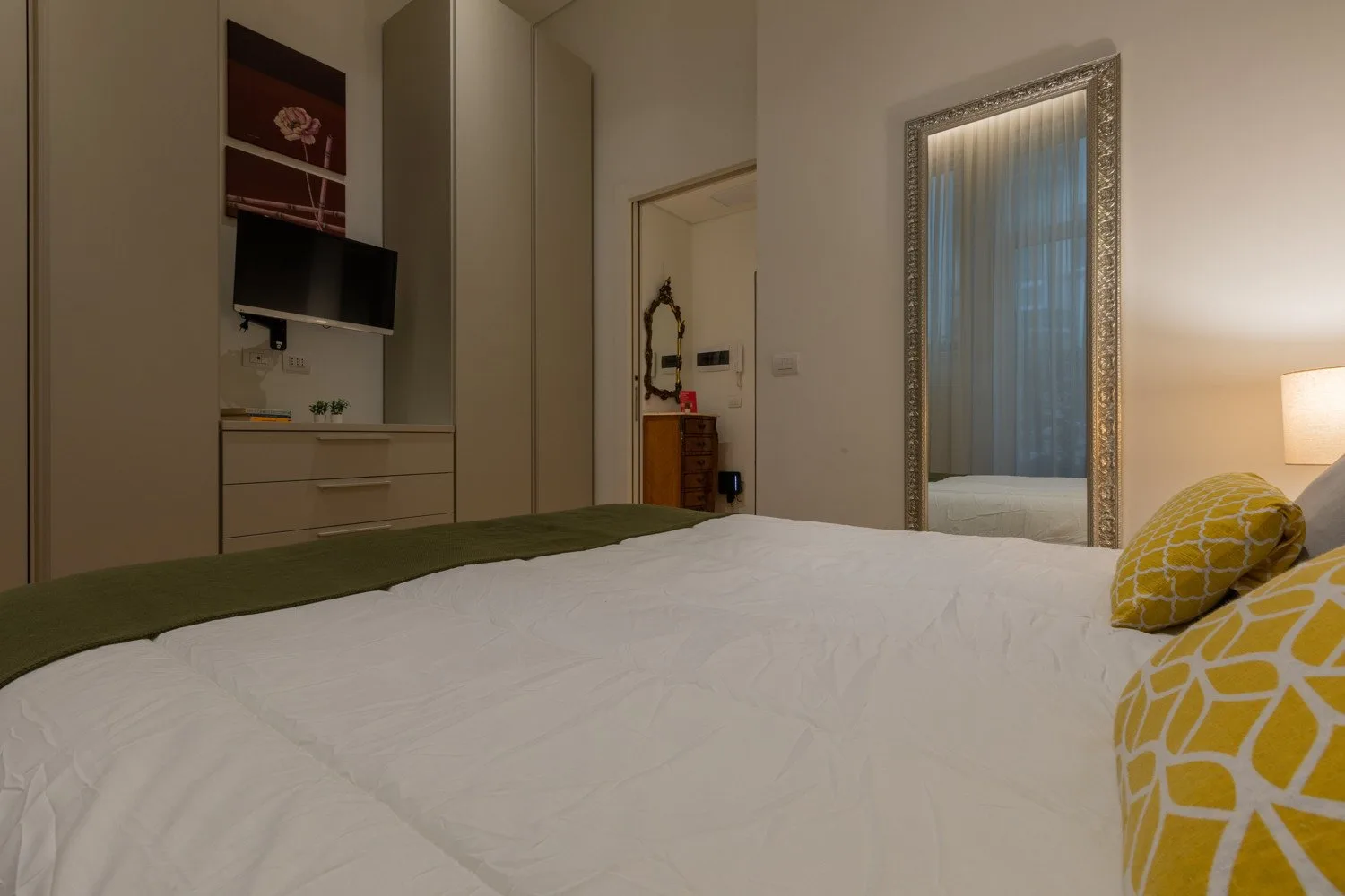 Un dormitorio con una cama bien tendida y almohadas amarillas estampadas.