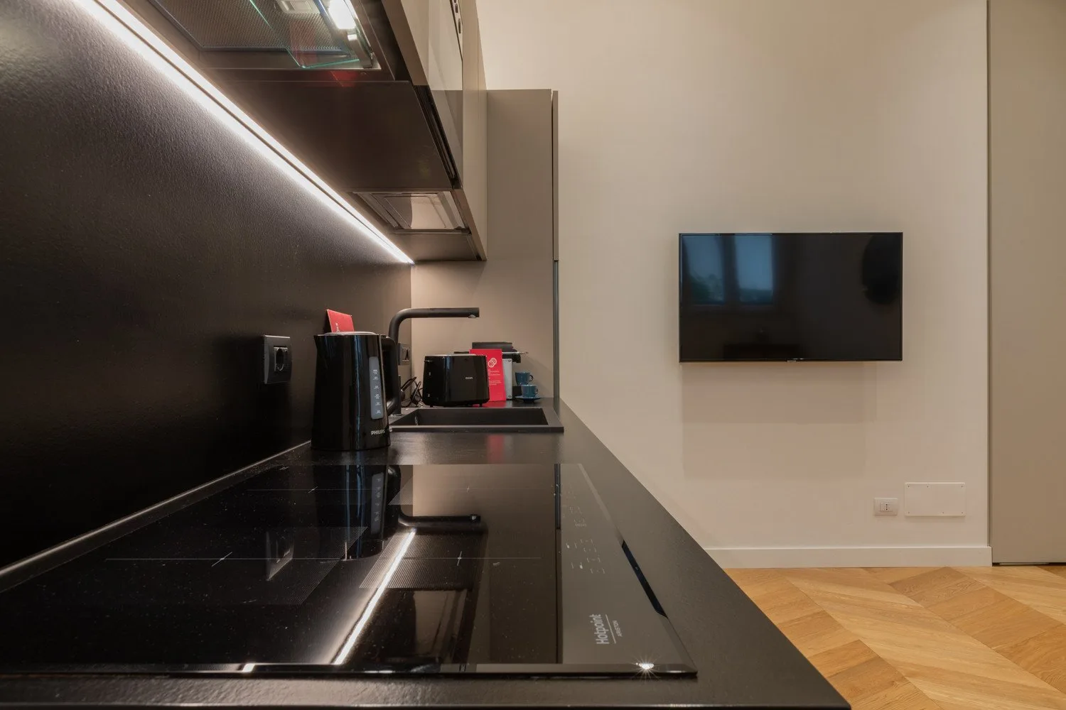 Una cocina pequeña moderna con una encimera oscura y un televisor montado en la pared.