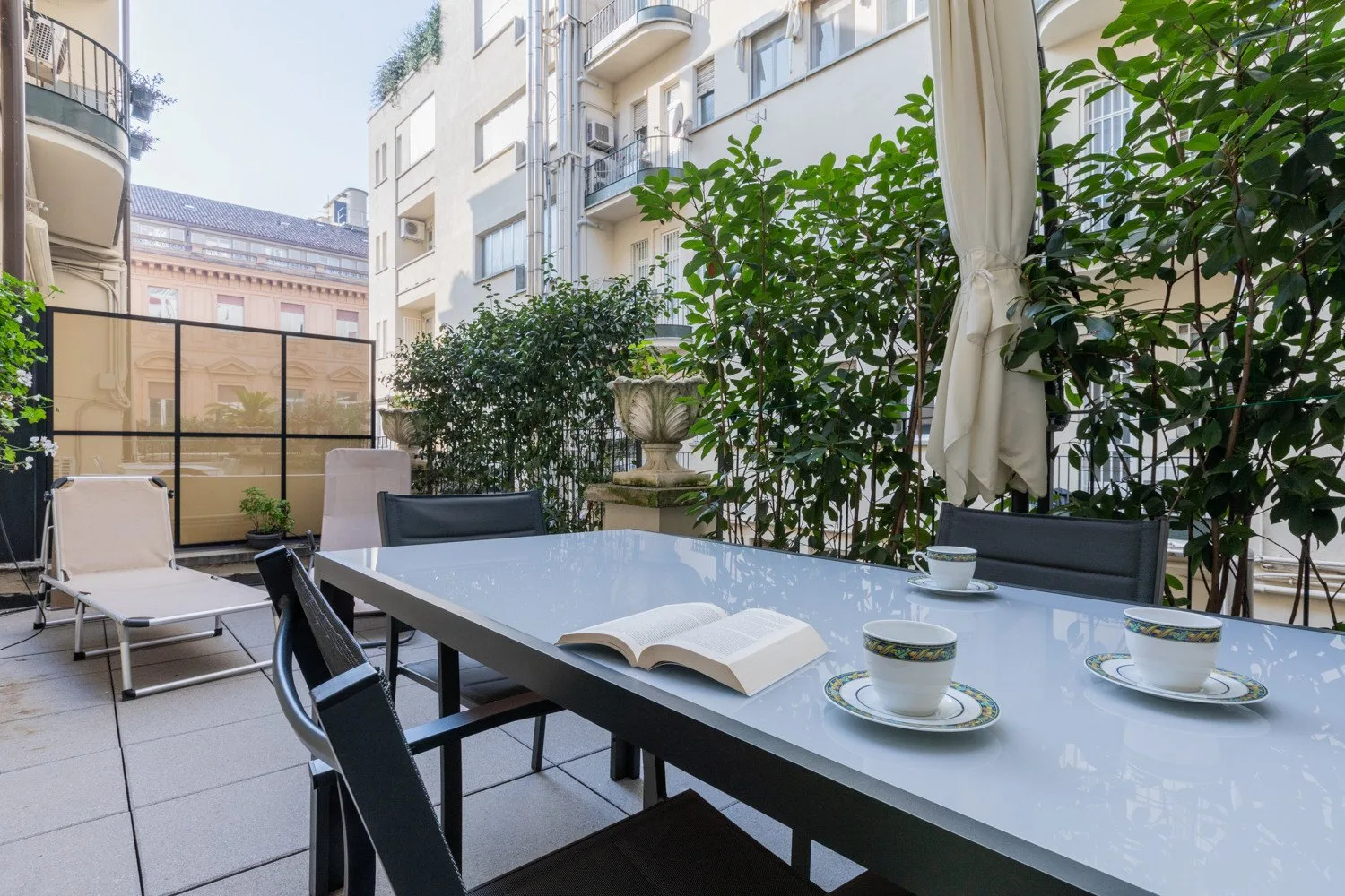 Un comedor al aire libre con una mesa larga, asientos y vegetación alrededor.