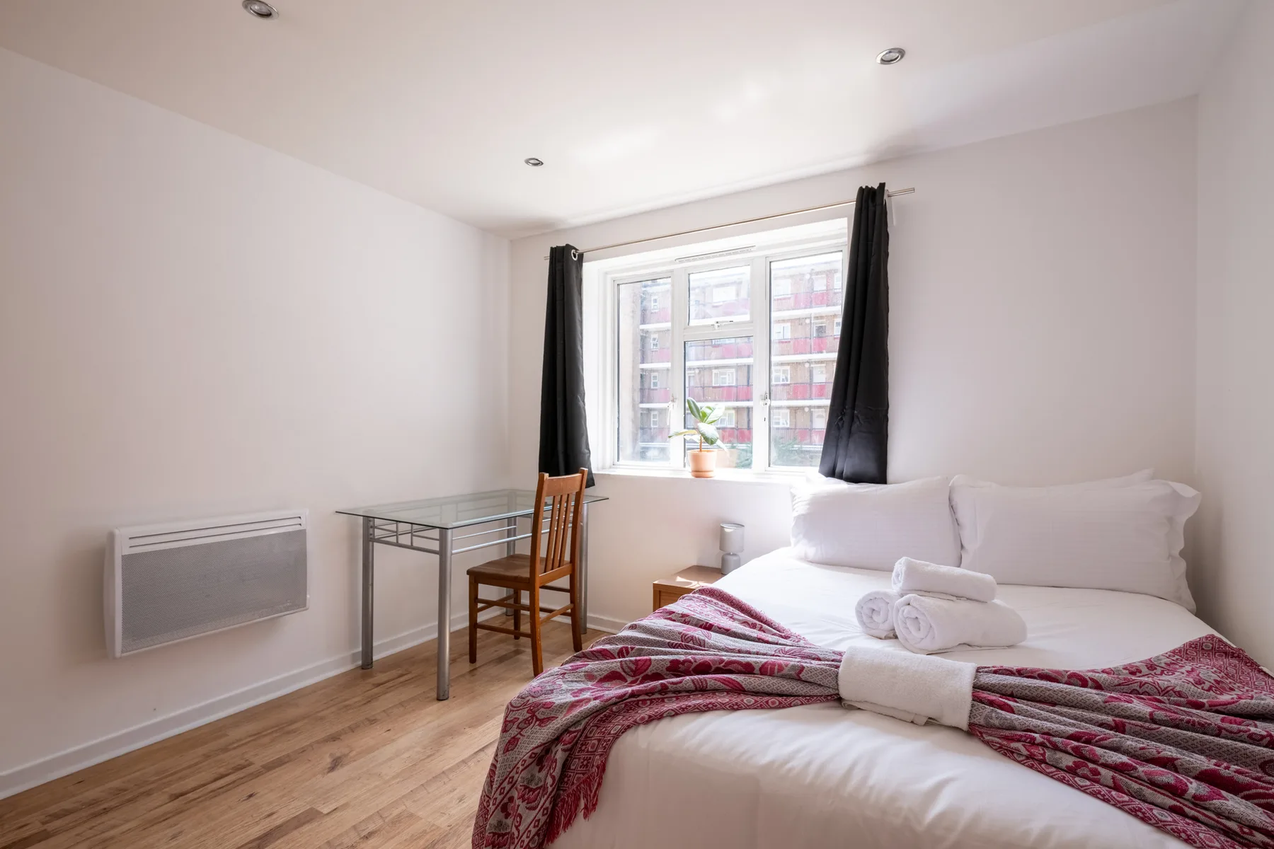 Un dormitorio luminoso con una cama, un escritorio pequeño y una ventana.
