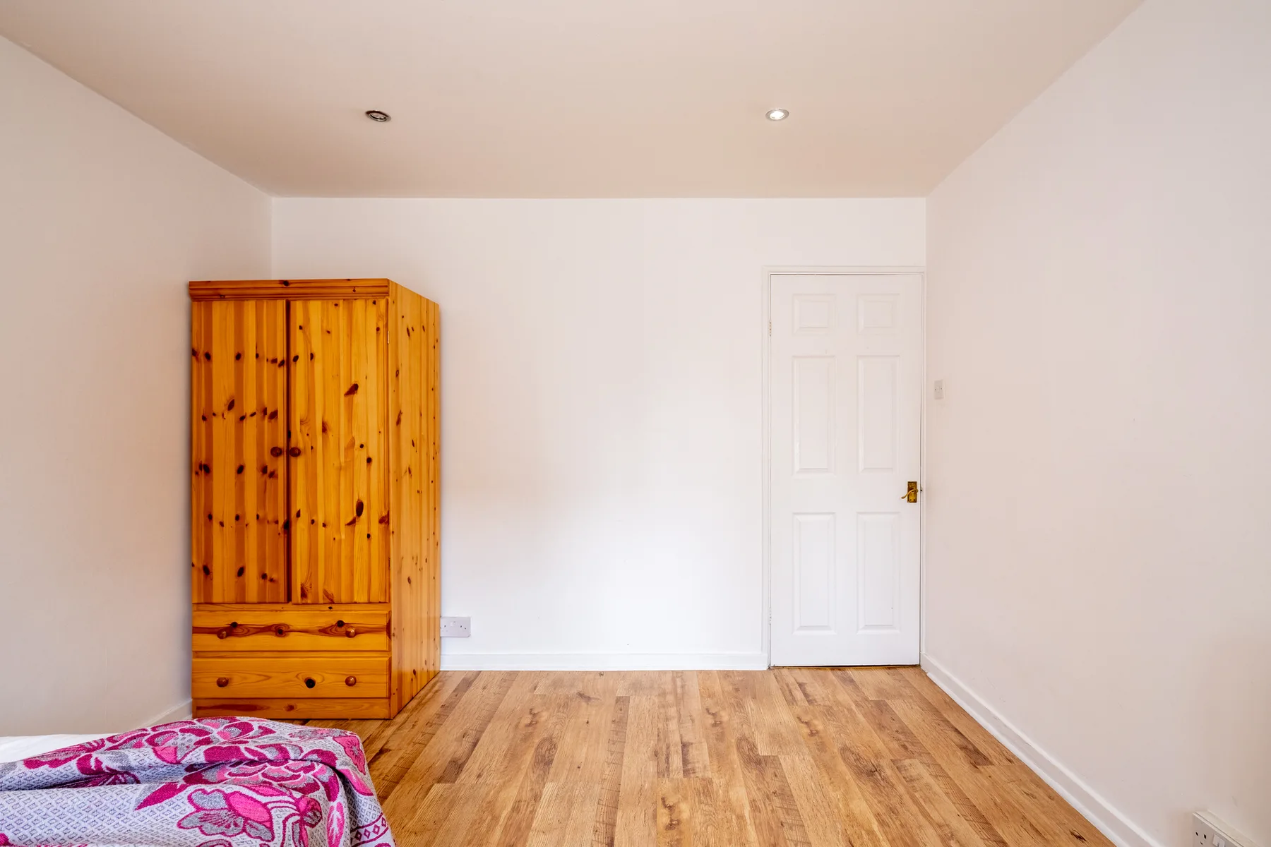 Un dormitorio sencillo con un armario de madera y una esquina de la cama.
