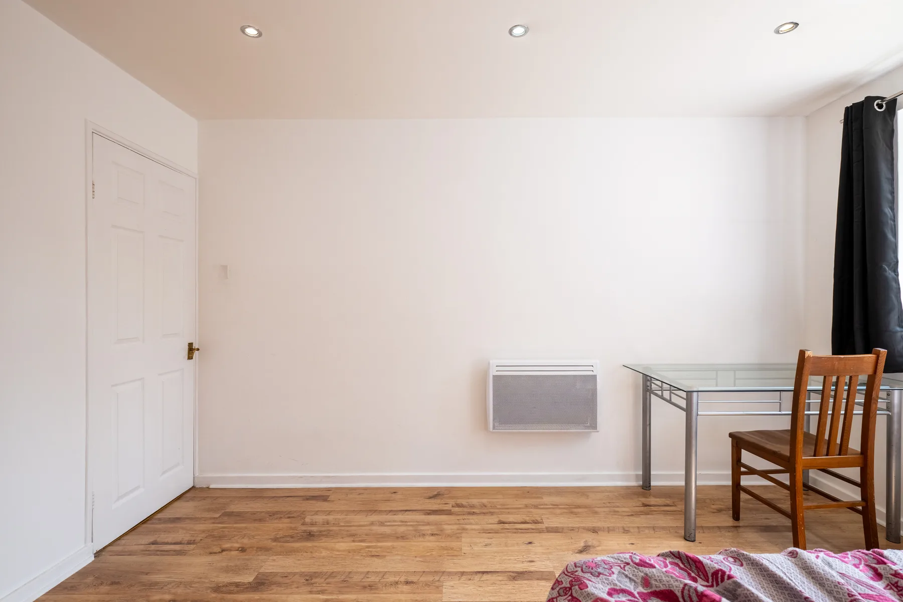 Una habitación sencilla con una mesa pequeña, una silla y un calefactor en la pared.