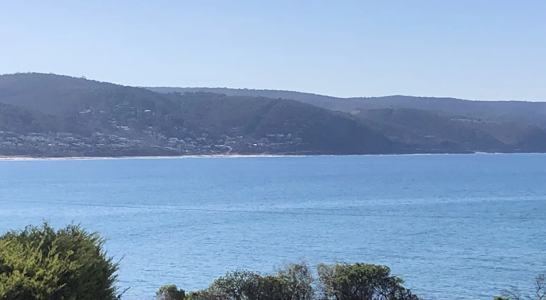 Una bahía costera con aguas azules tranquilas y colinas en la costa lejana.