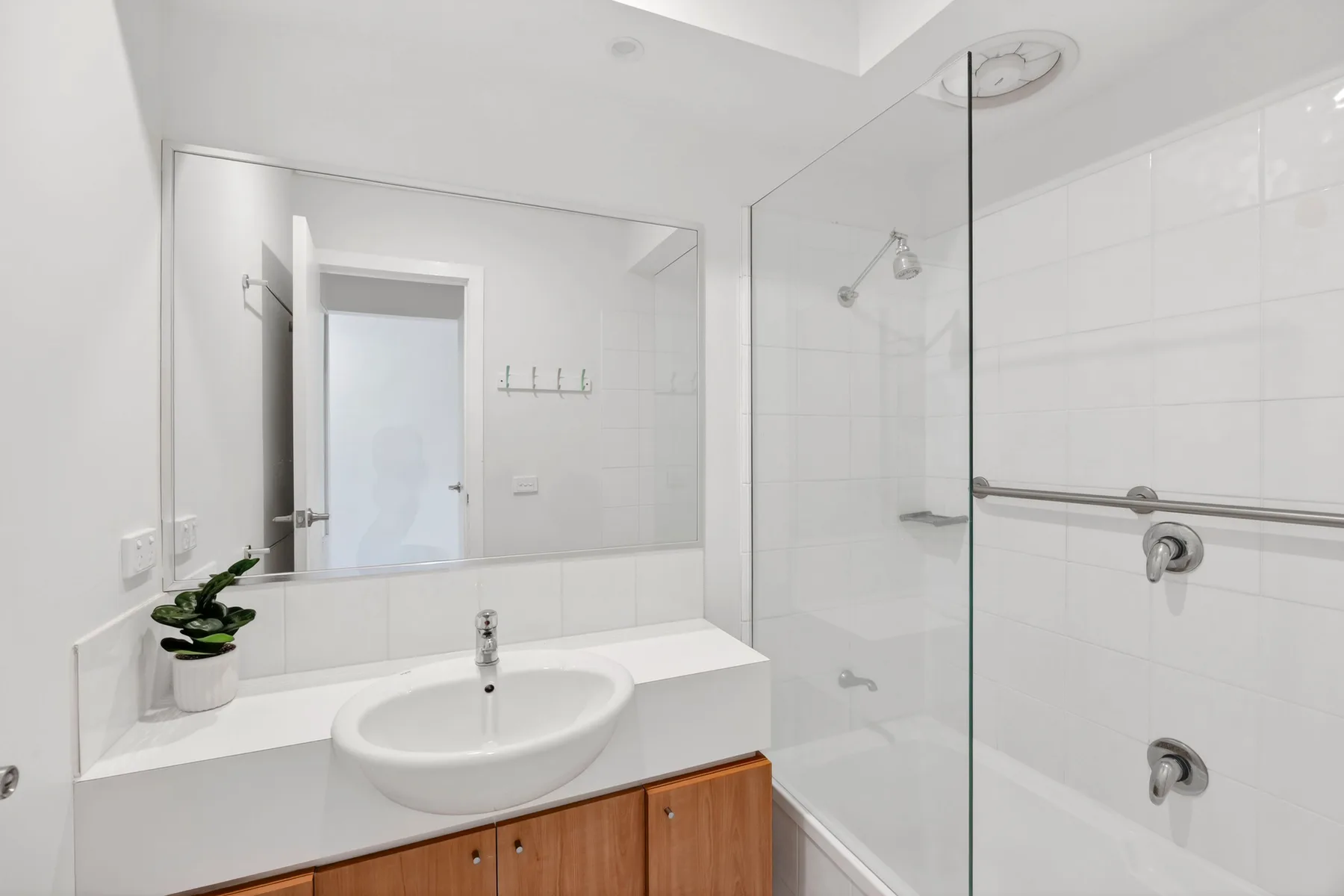 Un baño luminoso con lavabo blanco, espejo y ducha de cristal.