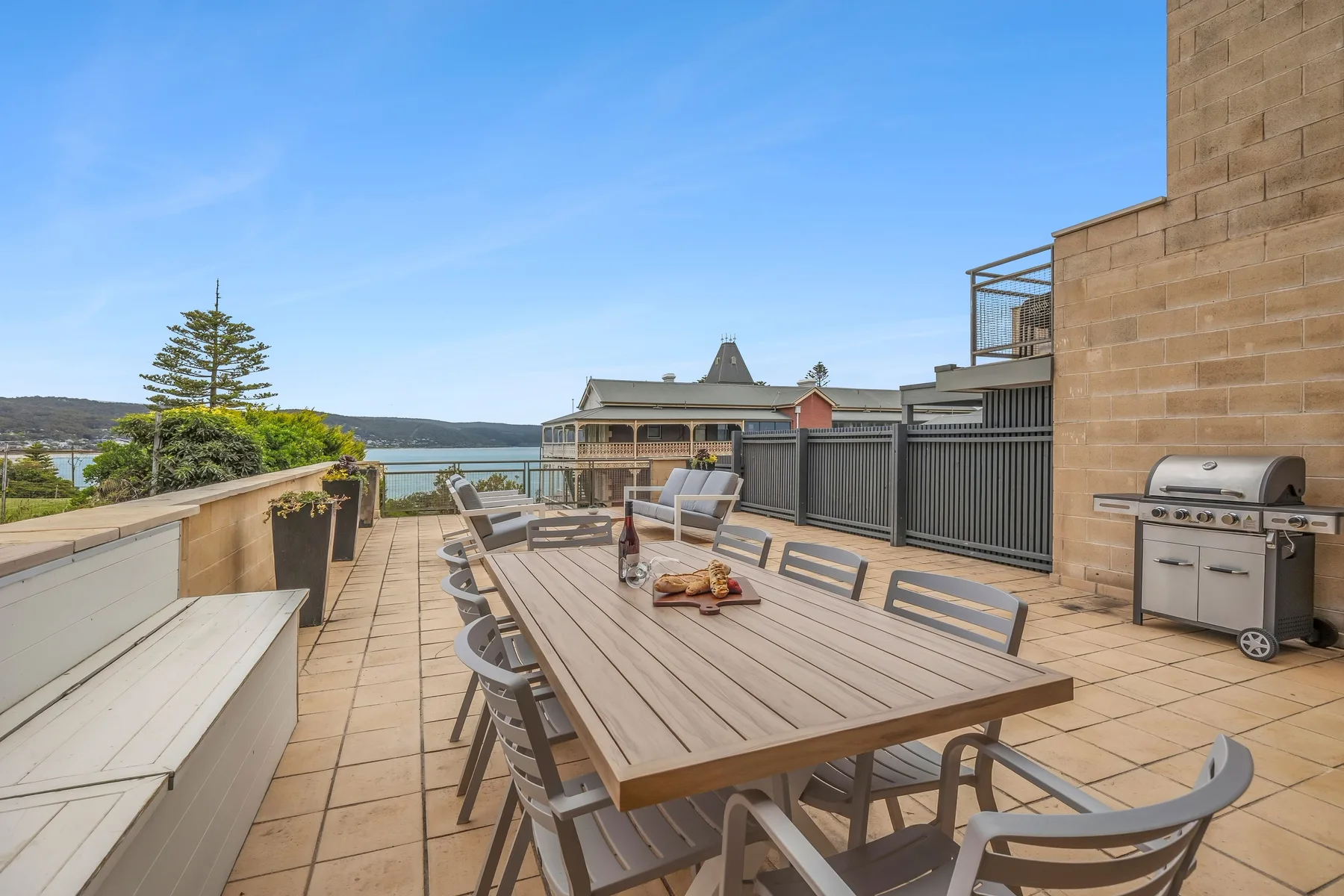 A rooftop terrace has a long dining table and chairs overlooking the water.