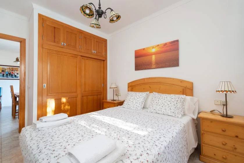 Un dormitorio con una cama doble, armarios de madera y una imagen de un atardecer sobre la cama.