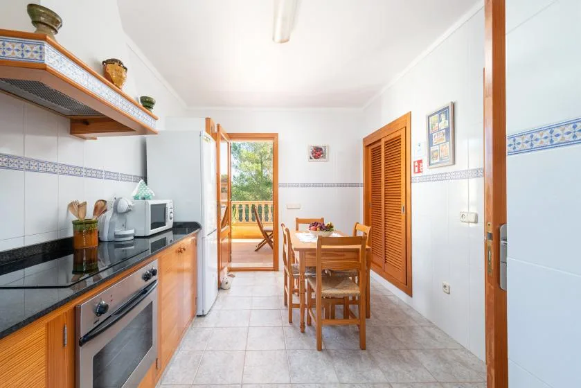 Una cocina alicatada con una mesa de comedor y una puerta abierta a un balcón.