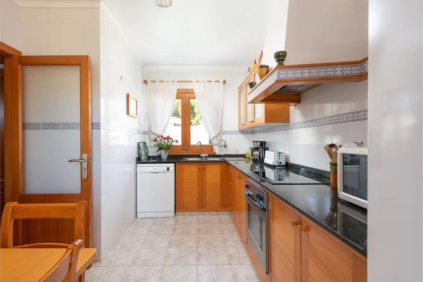 Una cocina luminosa con armarios de madera, encimeras oscuras y una ventana sobre el fregadero.