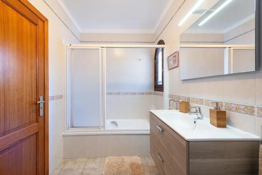 Un baño luminoso con bañera, mampara de ducha de vidrio y lavabo.