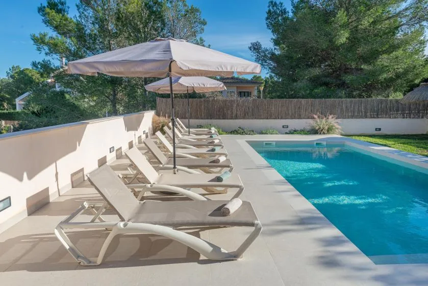 Poolside patio with lounge seating and umbrellas beside a swimming pool.