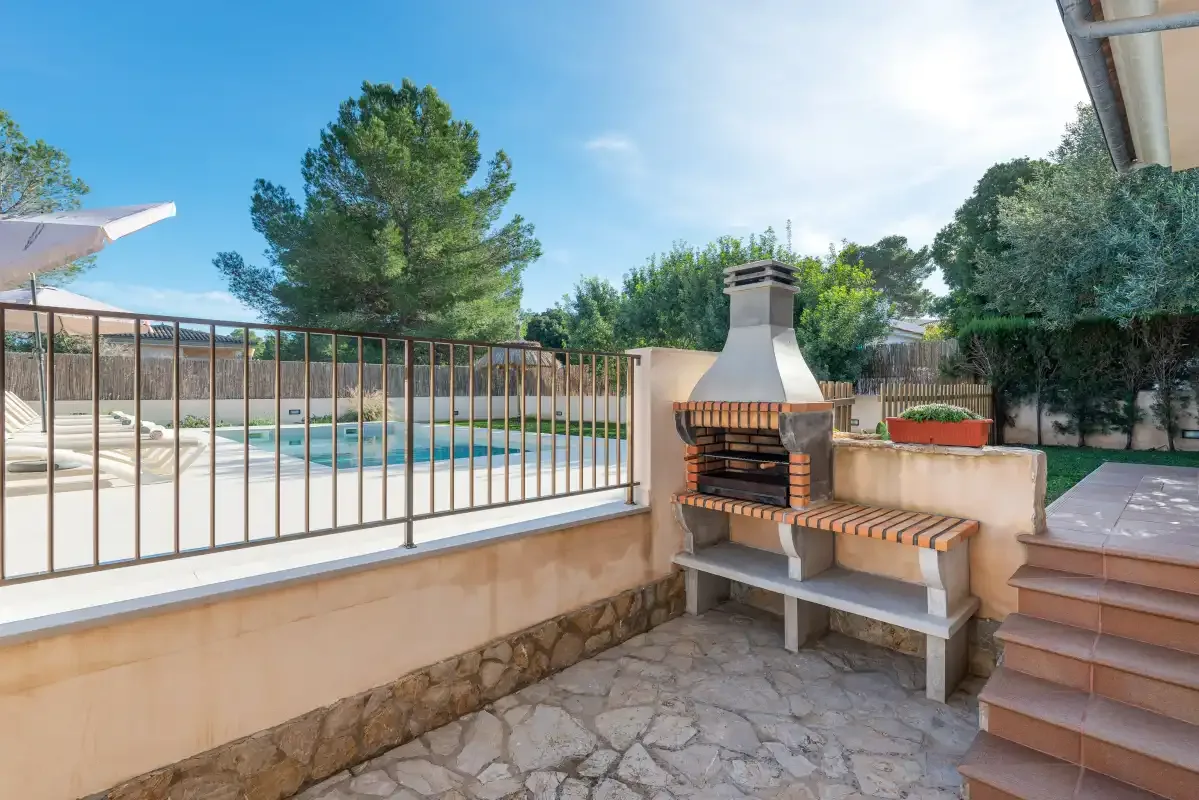 Un patio de piedra da a una piscina, con una barbacoa junto a los escalones.