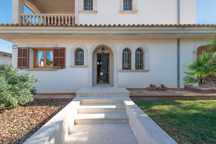 Entrada de una casa con escalones de piedra, ventanas arqueadas y un pequeño jardín.