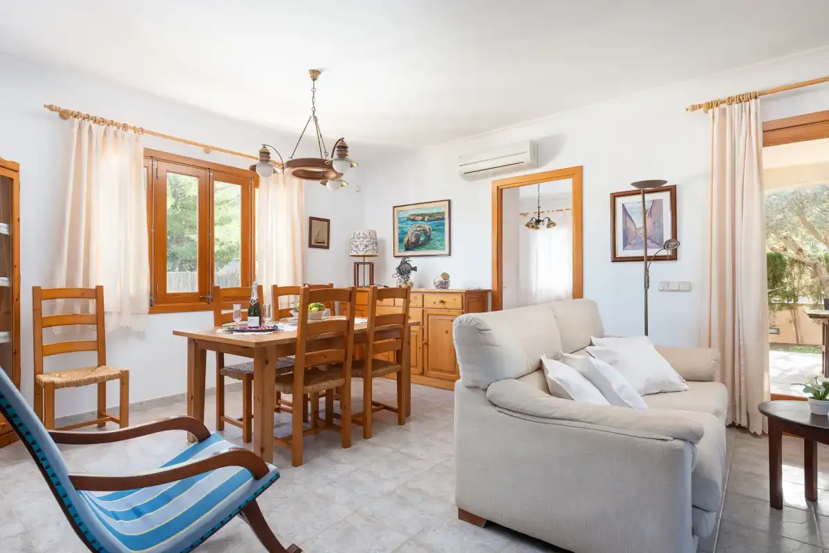 Sala de estar y comedor con asientos, una mesa de madera y ventanales.