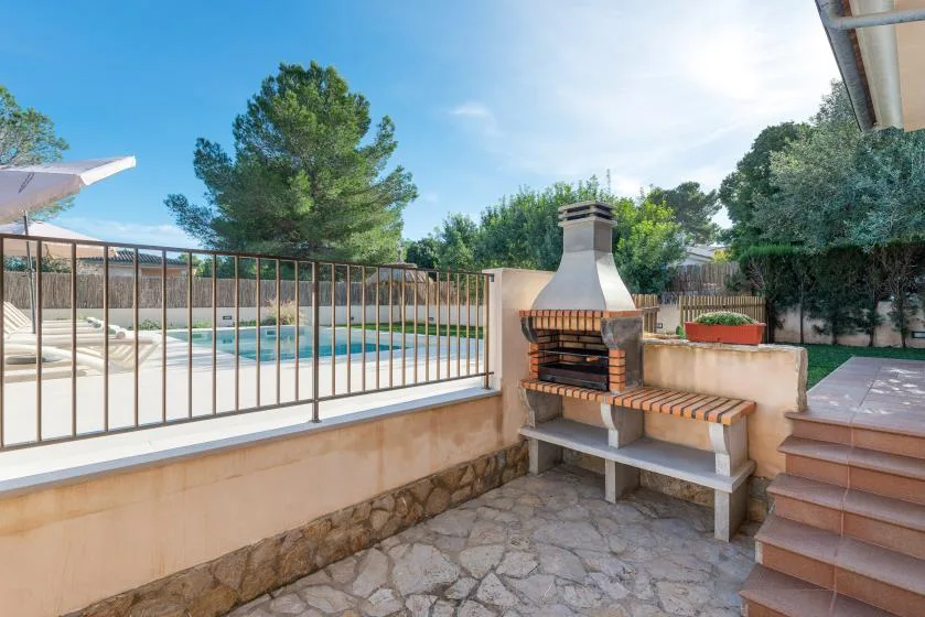 Un patio de piedra con una barbacoa de ladrillo al aire libre da a una piscina cercada.