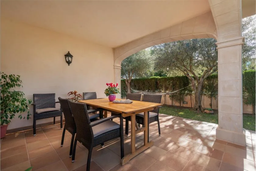A covered patio with a dining table and seating overlooks a leafy garden.